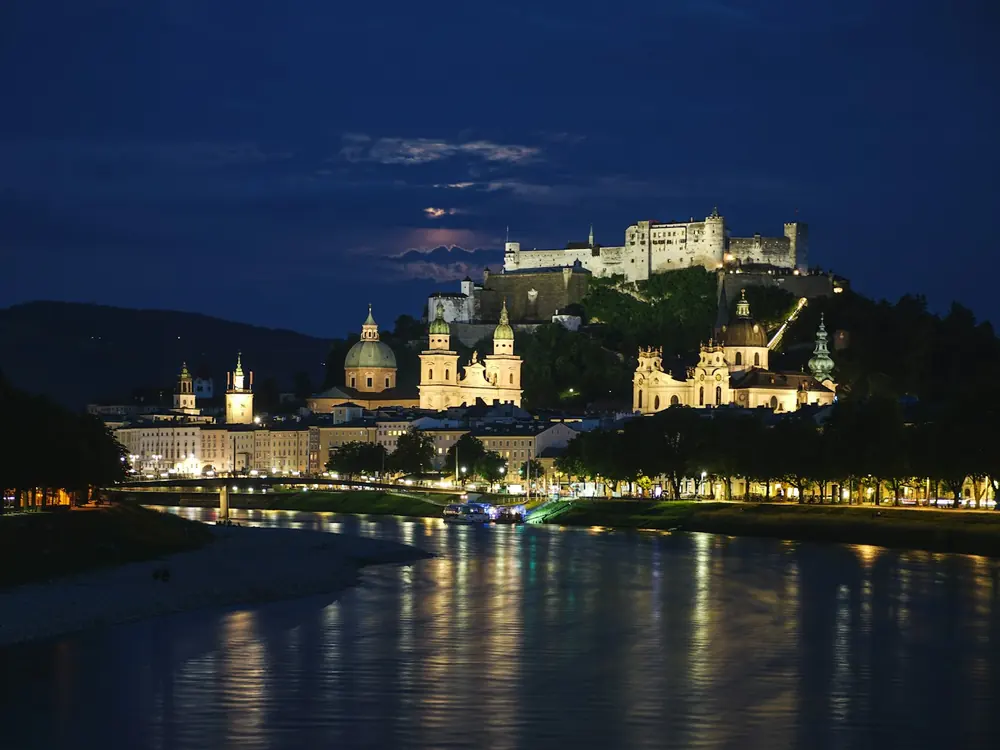 Hohensalzburg Fortress lit up at night above Salzburg's old town and the river Salzach